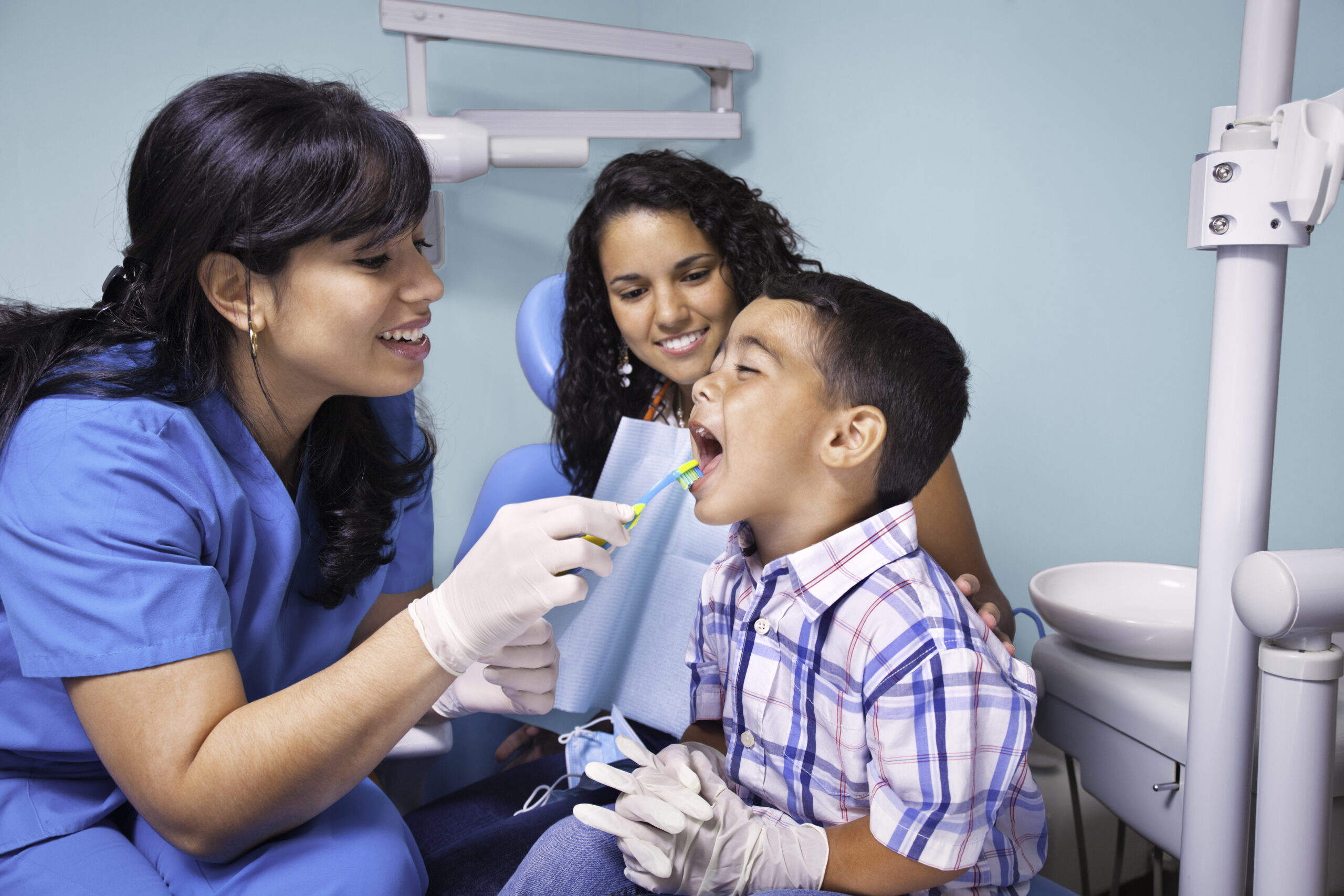 Hispanic dentist and mother teaching child use of toothbrush